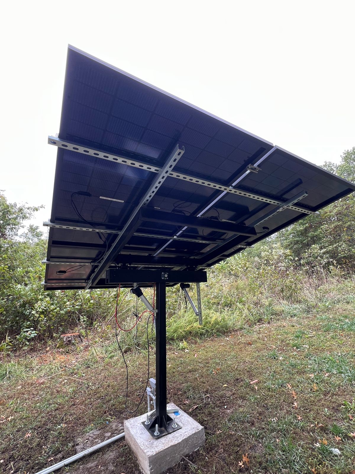 Underside of a finished tracker: strut rails under the bifacial panels and the linear actuators either side of the mast