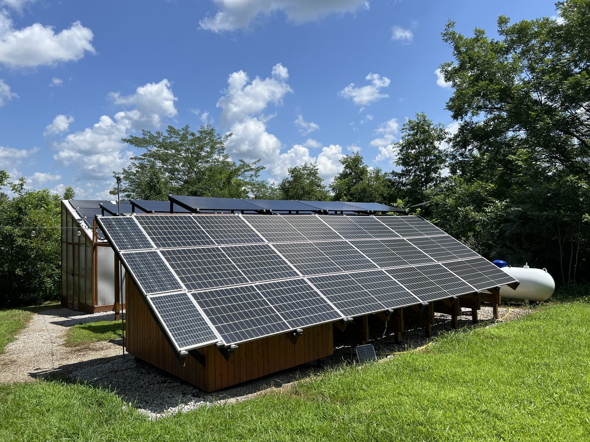 Ground mount and carport solar arrays with greenhouse in background